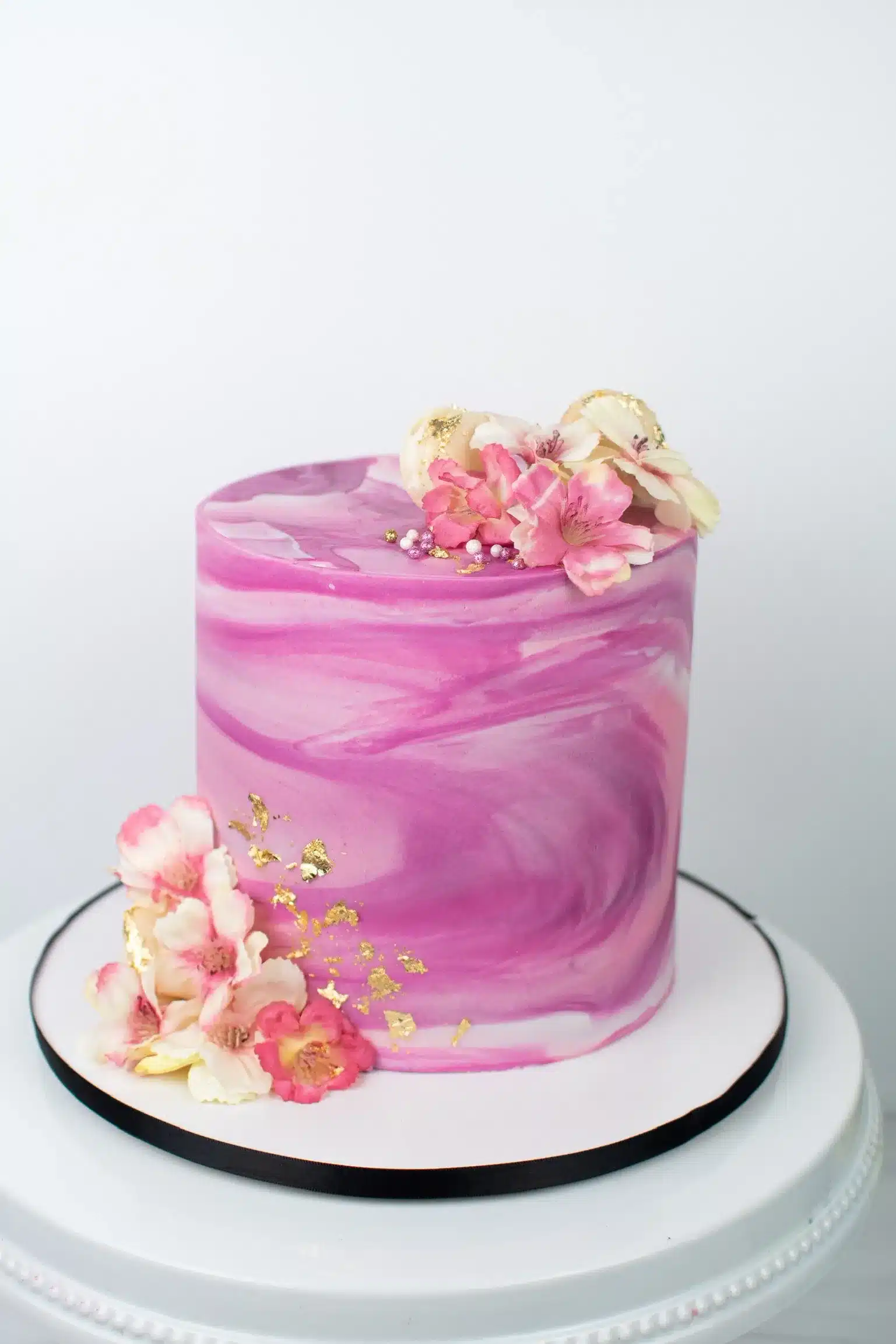 Single-tier cake with pink marbled fondant finish and pink floral decorations.