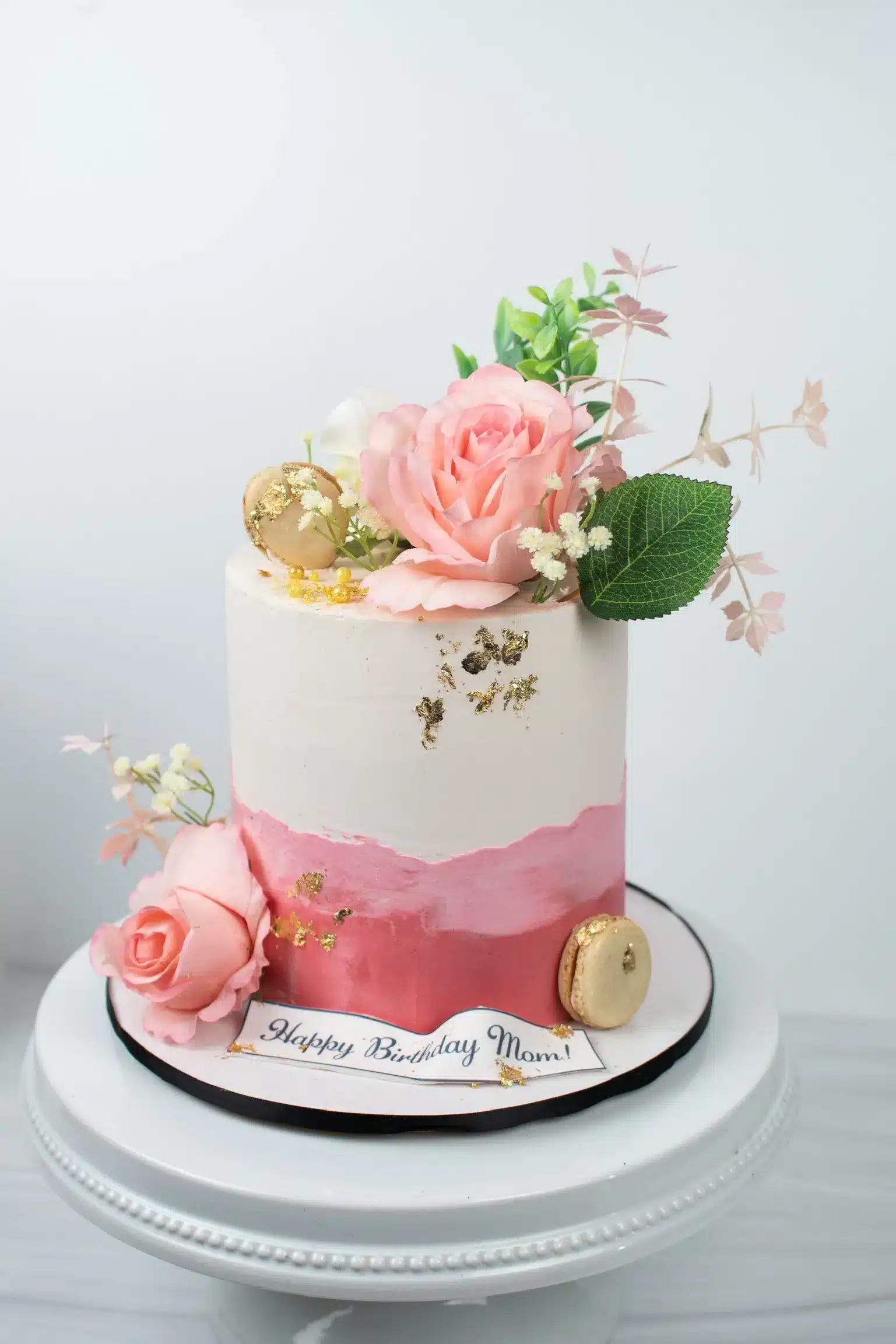Tiered white buttercream cake with pink gradient and edible flower decoration, perfect for weddings or special occasions.