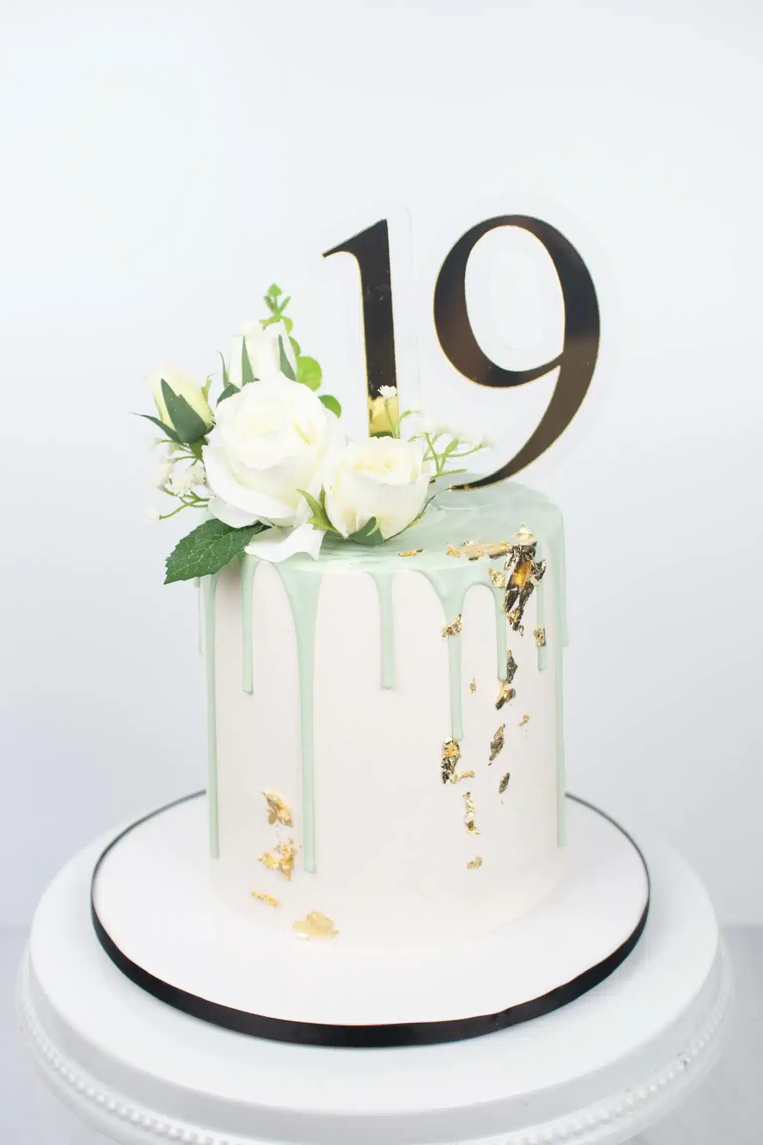 White buttercream cake with gold accents, topped with fresh white flowers and a '19' topper, ideal for milestone celebrations.